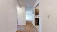 Located on Belmont Street in Liberty, Missouri, this 2-bedroom, 1-bathroom residence offers a practical and comfortable single-floor layout. The living room serves as the centerpiece of the home, showcasing a full-wall brick fireplace with a wood mantel and built-in shelving on either side. Plush wall-to-wall carpeting, a textured ceiling, and a ceiling fan complete the space. Sliding glass doors open to a private balcony, allowing natural light to fill the room and providing outdoor views of the surrounding community. The kitchen features rich dark wood cabinetry and tile flooring, accessible via a pass-through window from the living area. A connecting hallway leads to both bedrooms, each carpeted and equipped with ample closet space. The primary bedroom offers two separate closets with shelving for generous storage. The second bedroom includes a window that brings in natural light. The shared full bathroom features a white vanity with cabinet storage, dual framed mirrors, and tile flooring. A central hallway with a louvered closet door provides additional organizational space, tying together the efficient and functional floor plan of this Liberty, MO residence.