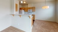 This single-floor residence offers a thoughtfully designed layout that balances functionality and comfort throughout. The kitchen is a standout feature, outfitted with warm honey-toned wood cabinetry, light-colored countertops, white appliances including a range, microwave, and refrigerator, and durable hardwood-style flooring. A peninsula with bar-height seating extends into the living area, creating a seamless open-concept flow ideal for everyday living and entertaining.

The living area is generously sized, with plush neutral carpeting and large windows that allow ample natural light to fill the space. A sliding glass door opens directly to a private outdoor patio, offering views of the surrounding neighborhood. The bedrooms continue the warm, neutral palette with soft carpeting, bright windows fitted with blinds, and closet access, providing comfortable and practical retreats.

Two bathrooms serve the unit. One features warm terracotta-toned tile flooring, a combination tub and shower, and a wood-framed vanity with mirror. The second bathroom offers a glass-enclosed walk-in shower, a built-in wood storage cabinet, a window for natural light, and matching tile flooring with a coordinating vanity. Together, the spaces present a cohesive, clean aesthetic throughout.