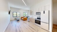 Located at 440 Monroe Ave in downtown Memphis, TN, this efficiently designed one-bedroom, one-bathroom unit offers a thoughtfully organized single-floor layout. The open-concept living and kitchen area is bright and welcoming, featuring light hardwood floors that run throughout the space and crisp white walls that enhance the sense of openness. Elevated linear lighting runs across the ceiling, complementing the natural light that pours in through multiple black-framed windows overlooking greenery outside.

The kitchen is equipped with white cabinetry, open shelving, light wood lower cabinets, a stainless steel dishwasher, microwave, and a white electric range — all positioned along a clean, functional countertop with a built-in sink. Adjacent to the kitchen, the living area offers comfortable space for a seating arrangement.

The bedroom is a generous, well-proportioned retreat with high ceilings, white walls, and light hardwood flooring. A wall-mounted flat-screen television and decorative wall art add character to the room, which connects directly to the bathroom.

The bathroom features a full tub-shower combo with white tile surround, hardwood flooring, and a vanity with storage. Notably, a stacked washer and dryer unit is conveniently housed within the bathroom, providing in-unit laundry — a practical and valuable feature.