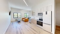 Located at 440 Monroe Ave in downtown Memphis, TN, this efficiently designed one-bedroom, one-bathroom unit offers a thoughtfully organized single-floor layout. The open-concept living and kitchen area is bright and welcoming, featuring light hardwood floors that run throughout the space and crisp white walls that enhance the sense of openness. Elevated linear lighting runs across the ceiling, complementing the natural light that pours in through multiple black-framed windows overlooking greenery outside.

The kitchen is equipped with white cabinetry, open shelving, light wood lower cabinets, a stainless steel dishwasher, microwave, and a white electric range — all positioned along a clean, functional countertop with a built-in sink. Adjacent to the kitchen, the living area offers comfortable space for a seating arrangement.

The bedroom is a generous, well-proportioned retreat with high ceilings, white walls, and light hardwood flooring. A wall-mounted flat-screen television and decorative wall art add character to the room, which connects directly to the bathroom.

The bathroom features a full tub-shower combo with white tile surround, hardwood flooring, and a vanity with storage. Notably, a stacked washer and dryer unit is conveniently housed within the bathroom, providing in-unit laundry — a practical and valuable feature.