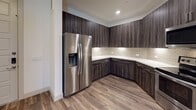 This single-floor residence showcases a thoughtfully designed interior with a cohesive modern aesthetic throughout. The kitchen is a standout feature, outfitted with rich dark wood-grain cabinetry extending from floor to ceiling, crisp white quartz countertops, and a neutral subway tile backsplash. Stainless steel appliances — including a side-by-side refrigerator with an ice and water dispenser, an electric range, and an over-the-range microwave — complete the fully equipped culinary space. Wood-look plank flooring runs through the kitchen and main living areas, lending warmth and continuity to the open layout. The living space benefits from natural light through slatted blinds and provides direct access to an exterior door, while ceiling fans in multiple rooms enhance comfort and airflow. The carpeted bedrooms offer a softer, quieter retreat, with one bedroom featuring access to a walk-in closet with built-in shelving for generous storage. The bathroom is finished with large-format tile surrounding a soaking tub and shower combination, a dark wood vanity with a quartz countertop, and a framed mirror — all reflecting the same refined design language found throughout the home. The overall ambiance is clean, contemporary, and move-in ready.