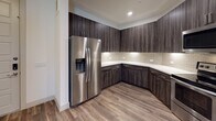 This single-floor residence showcases a thoughtfully designed interior with a cohesive modern aesthetic throughout. The kitchen is a standout feature, outfitted with rich dark wood-grain cabinetry extending from floor to ceiling, crisp white quartz countertops, and a neutral subway tile backsplash. Stainless steel appliances — including a side-by-side refrigerator with an ice and water dispenser, an electric range, and an over-the-range microwave — complete the fully equipped culinary space. Wood-look plank flooring runs through the kitchen and main living areas, lending warmth and continuity to the open layout. The living space benefits from natural light through slatted blinds and provides direct access to an exterior door, while ceiling fans in multiple rooms enhance comfort and airflow. The carpeted bedrooms offer a softer, quieter retreat, with one bedroom featuring access to a walk-in closet with built-in shelving for generous storage. The bathroom is finished with large-format tile surrounding a soaking tub and shower combination, a dark wood vanity with a quartz countertop, and a framed mirror — all reflecting the same refined design language found throughout the home. The overall ambiance is clean, contemporary, and move-in ready.