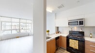 This contemporary two-floor residence offers a clean, modern aesthetic defined by crisp white walls, light wood-tone flooring, and an abundance of natural light throughout. The open-concept main level connects the living area and kitchen seamlessly, creating an inviting and functional flow. The kitchen is well-appointed with warm wood cabinetry paired with white upper cabinets and light countertops, stainless steel appliances including a refrigerator and over-the-range microwave, a gas range, dishwasher, and a stainless steel sink — all designed for both style and practicality. The living area on the main floor benefits from large floor-to-ceiling windows that frame urban views and bathe the space in natural light, complemented by a baseboard heating unit beneath the windows. A striking staircase with a sleek stainless steel and wood railing connects the two floors, serving as an architectural focal point. The upper level offers additional living space with its own open layout and access to a full bathroom featuring a tiled tub-shower combo. The main floor also includes a stylish half bath with a vessel sink, dark wood vanity, and a modern wall-mounted mirror. Throughout, the light flooring and neutral palette create a bright, airy ambiance suited to a variety of lifestyles.