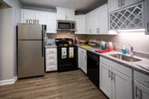 Located at 6315 Kingston Pike in Knoxville, Tennessee, this single-floor residence offers a well-designed layout with a thoughtful blend of updated finishes and practical living spaces. The kitchen stands out as a highlight, featuring crisp white shaker cabinetry, granite countertops, a subway tile backsplash with a decorative diamond-pattern accent, stainless steel appliances including a dishwasher and microwave, and durable wood-look flooring that adds warmth to the space. The living area is generously sized, finished with plush carpeting, crown molding, and a striking barn-style sliding door. French doors open to an outdoor area, inviting natural light and providing a seamless indoor-outdoor connection. The bedrooms are comfortably proportioned, each featuring soft carpeting, neutral gray walls, and windows fitted with blinds that allow for natural light. The primary bedroom includes access to a walk-in closet and an en-suite bathroom. The bathrooms are well-appointed, with one showcasing a dual-sink granite vanity with modern pendant lighting, and another featuring a classic white subway tile tub-and-shower surround. Textured ceilings are present throughout, and the overall color palette of soft grays and whites creates a clean, contemporary ambiance across the entire unit.
