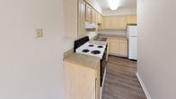 This single-floor residence offers a practical and comfortable layout designed for everyday living. The kitchen is well-appointed with light wood cabinetry providing ample storage, laminate countertops, a double-basin sink, and white appliances including a coil-burner range and refrigerator. Dark wood-style vinyl plank flooring runs through the kitchen, adding warmth and durability to the space.

The full bathroom features white tile surrounding a combination tub and shower, a single vanity with sink, and the same dark wood-style vinyl plank flooring found in the kitchen. A window with blinds allows for natural light while maintaining privacy.

The living area is generously sized, carpeted in a neutral tone, and fitted with a ceiling fan with integrated lighting. Large vertical blinds cover a sliding glass door, and an additional window invites natural light and outdoor views. The space flows openly, offering flexibility for various furniture arrangements.

The bedroom is bright and airy, featuring plush carpet, a window with blinds that frames natural light, and clean white walls that create a calm and restful atmosphere. The overall design of the residence is clean and straightforward, with a neutral palette that provides a versatile canvas for personalization.