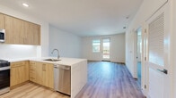 Located at 1205 Aviara Parkway in Carlsbad, CA, this thoughtfully designed one-bedroom, one-bathroom residence offers a bright, modern living experience across a single floor. Light-toned hardwood-style flooring flows seamlessly throughout, complementing the clean white walls and creating a cohesive, airy aesthetic.

The open-concept kitchen and living area serves as the heart of the home. The kitchen is outfitted with warm natural wood cabinetry, stainless steel appliances including a gas range, refrigerator, and microwave, as well as a striking quartz waterfall island with an undermount sink — ideal for both meal preparation and casual dining. Recessed lighting enhances the functional elegance of the space.

The living area opens to a private balcony through a glass-panel door, inviting natural light and outdoor views into the home. The generously sized bedroom features large windows, continuing the bright, open feel, and connects to a dedicated walk-in closet equipped with built-in shelving and hanging rods for ample storage.

The full bathroom is finished with large-format tile flooring, a tub-shower combination with white subway tile surround, a wood-toned vanity, and a quartz countertop, maintaining the modern design language found throughout the residence.