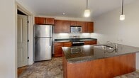This well-appointed 2-bedroom, 2-bathroom residence at 4001 E Genesee St in Syracuse, NY offers a thoughtfully designed single-floor layout. The open-concept kitchen flows seamlessly into the living area, creating a cohesive and functional living space. The kitchen is equipped with rich cherry wood cabinetry, dark granite countertops, stainless steel appliances including a refrigerator, range, microwave, and dishwasher, complemented by pendant lighting and tile flooring. The living area extends from the kitchen peninsula and features light hardwood-style flooring and a window that brings in natural light. Both bedrooms continue the hardwood-style flooring and are bathed in natural light through windows with views of the surrounding neighborhood. The generously sized primary bedroom features dual windows, while the second bedroom offers a quieter, more intimate feel. Each bathroom is finished with warm-toned tile flooring, rich cherry wood vanities, arched mirrors with accent lighting, and a tiled shower. Additional conveniences include a dedicated laundry room, two closets, and a connecting hallway. The neutral color palette throughout creates a clean, inviting ambiance.