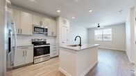 This well-appointed 1-bedroom, 1-bathroom unit is thoughtfully designed with a modern aesthetic and a cohesive, neutral color palette throughout. The open-concept kitchen and living area serves as the heart of the space, anchored by a central island with granite countertops and a black matte sink — ideal for both meal preparation and casual dining. The kitchen is outfitted with stainless steel appliances, including a refrigerator with ice maker, electric range, over-the-range microwave, and dishwasher. Crisp white subway tile backsplash and soft gray cabinetry with matte black hardware complete the contemporary kitchen design. Light wood-style flooring extends seamlessly through the main living areas and bedroom, contributing to a bright, airy feel. Recessed lighting and a ceiling fan enhance the living area, which also benefits from a window allowing in natural light. The bedroom is a comfortable, well-proportioned retreat featuring its own ceiling fan and a window with exterior views. The bathroom includes a granite-topped vanity with matching cabinetry, a soaking tub with tile surround, and direct access to a dedicated closet with built-in shelving — providing convenient and organized storage.