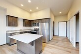 Located at 1011 S Laventure Rd in Mount Vernon, Washington, this thoughtfully designed single-floor studio makes efficient use of its space through modern finishes and a smart open layout. Light-toned luxury vinyl plank flooring runs throughout, lending a clean, cohesive feel to the entire unit.

The kitchen is the centerpiece of the space, showcasing rich dark-stained cabinetry with ample storage, a tile mosaic backsplash, and white quartz countertops. A center island provides additional prep and casual dining space. The full suite of stainless steel appliances—including a refrigerator, electric range, microwave, and dishwasher—ensures full functionality. Recessed lighting above enhances the modern aesthetic, while notably tall ceilings give the kitchen a more expansive, airy feel.

The open living area benefits from a large sliding glass door that floods the space with natural light and leads to a private balcony overlooking lush greenery. A dedicated closet with built-in shelving provides valuable storage. The bathroom features dark cabinetry paired with light countertops, and includes a stacked washer/dryer unit for added convenience, along with an accessibility grab bar. Neutral wall tones throughout tie the design together, creating a clean and welcoming ambiance.