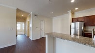 This single-story residence presents a well-appointed open-concept layout that seamlessly connects the main living areas. The living space is anchored by rich, dark hardwood-style flooring that extends throughout the common areas, complemented by crown molding details and recessed lighting overhead. Decorative columns frame the transition between the entry and living areas, adding architectural character to the space.

The kitchen is a standout feature, equipped with rich dark-wood cabinetry, granite countertops, a subway tile backsplash, and a full suite of stainless steel appliances including a refrigerator, range, microwave, and dishwasher. A peninsula with a granite countertop provides additional workspace and serves as a natural divider between the kitchen and living areas.

The bedrooms offer plush wall-to-wall carpeting, ceiling fans, and windows that allow natural light to fill each room. The bathroom is finished with neutral stone-look tile flooring and wall surround, a soaking tub, dark wood vanity cabinetry, and a granite countertop, creating a cohesive and refined aesthetic throughout the unit.