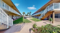 Located at 1908 Northwest 4th Avenue in Boca Raton, Florida, this compact single-room space is part of a two-story residential complex with a distinctive Florida architectural style. The building exterior, finished in warm yellow tones, features covered walkways and white-railed balconies that line both levels, providing sheltered access to each unit.

The complex is oriented around a well-maintained central courtyard, which serves as a defining feature of the property. Lush green lawns, tropical palm trees, and low-growing ornamental plantings create a verdant outdoor environment that brings natural character to the community. Concrete pathways connect the buildings, offering practical circulation throughout the grounds. The open-air courtyard allows for abundant natural light and a sense of openness characteristic of South Florida living.

The interior of the individual room is compact and self-contained, suited for a focused single-purpose use. While interior lighting in the captured imagery is limited, the unit is part of a building that benefits from its sunny Boca Raton location and the lush communal outdoor setting. The property's proximity to the amenities of downtown Boca Raton adds to its overall appeal, making it a practical and conveniently situated space within a well-established South Florida community.