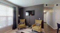 Located at 6667 Wesbury Park Ave in Columbus, OH, this single-floor residence offers a thoughtfully designed layout with a cohesive modern aesthetic. The living room serves as the heart of the home, anchored by a bold dark accent wall that contrasts with lighter neutral tones. Large windows dressed with dark curtains invite natural light, while the open sightline connects to the kitchen and dining areas, enhancing the sense of spaciousness. The kitchen is outfitted with rich dark cabinetry, granite-style countertops, a tile backsplash, and black appliances, all set on warm wood-look flooring that flows throughout the main living spaces. A dedicated home office provides a functional workspace with its own window for natural light and durable hardwood-style flooring. The bedroom is a serene retreat featuring plush carpeting, a natural color palette, and a window framed by deep-toned curtains. Two bathrooms complete the residence — one featuring a stand-up glass-enclosed shower with a dark vanity, and another with a tub and shower combination, both showcasing wood-look tile flooring and dark navy cabinetry with well-lit mirrors. The overall ambiance is contemporary and cohesive, with carefully curated contrasts between dark cabinetry, warm flooring, and neutral walls throughout.