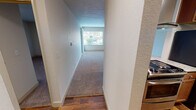 Located at 1300 S Puget Dr in Renton, Washington, Unit 306 is a single-floor residence offering a practical and functional layout. The entry transitions from hardwood-style flooring into a carpeted hallway that leads to the main living area. The living room is bright and open, benefiting from a large window that brings in natural light and offers views of the surrounding greenery. A wall-mounted air conditioning unit provides climate control for year-round comfort. The kitchen is well-appointed with warm wood cabinetry, granite-style countertops, a stainless steel refrigerator, and a range, all set atop hardwood-style flooring that adds warmth to the space. A dedicated bedroom features plush carpeting, clean white walls, and a quiet, neutral atmosphere well-suited for rest. The bathroom includes a full tub and shower combination with chrome fixtures and a clean, white surround. Textured ceilings are present throughout the unit, adding a classic residential character. The overall layout, as seen from the overhead dollhouse view, is efficient and well-organized, making thoughtful use of the available space. This unit offers a comfortable and move-in ready living environment in a convenient Renton location.