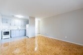 Located at 3300 Weston Rd in Toronto's northwest end, this 2-bedroom, 1-bathroom unit offers a practical and well-organized single-floor layout. The combined kitchen and living area forms the heart of the space, featuring warm parquet flooring that flows throughout. The kitchen is outfitted with grey cabinetry, granite-look countertops, a white stove, and a full-size refrigerator, complemented by light vinyl tile flooring. A ceiling-mounted light fixture brightens the area.

Both bedrooms carry the same parquet flooring and are served by radiator heating units positioned beneath wide windows. Natural light filters in through these windows, which frame views of surrounding trees and neighbouring buildings, giving each room a pleasant, connected-to-outdoors feel. One bedroom includes access to an outdoor balcony through a glass-panelled door.

The bathroom is clean and functional, finished in crisp white tile with a full-sized soaker tub and shower combination, a wall-mounted medicine cabinet, and a pedestal sink. Two hallways connect the rooms efficiently, maintaining a clear and logical flow throughout. The neutral colour palette of warm beige and white tones creates a calm, cohesive ambiance across the entire unit.