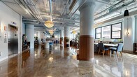 Located in the heart of Minneapolis's North Loop neighborhood, this single-floor space at 618 N Third St offers a striking blend of industrial heritage and contemporary design. The layout spans a generous open floor plan, characterized by polished concrete floors that reflect the abundant natural light streaming through large warehouse-style windows with black steel frames. Exposed brick walls, structural columns with warm wood-wrapped bases, and an overhead network of industrial ductwork and piping lend authentic character throughout.

The space is organized into a series of distinct yet connected zones. A welcoming entry area features a central elevator, reception counter, and tiered woven pendant lighting. The main gathering areas are furnished with a thoughtful mix of lounge seating—including velvet sofas, leather chairs, and area rugs—alongside communal tables and café-style bar seating with upholstered blue chairs. A connecting hallway with steel railings and exposed stone walls links the various wings of the space. Curated greenery, framed artwork, and decorative lighting fixtures add warmth and personality throughout. The overall ambiance is an inviting, sophisticated environment that balances the raw textures of its historic bones with refined, modern interiors.