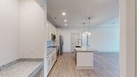 Located at The Sutton in Winston Salem, NC, this well-designed three-bedroom, two-bathroom residence offers a thoughtfully laid-out single-floor plan with contemporary finishes throughout. The open-concept kitchen and living area serves as the heart of the home, showcasing crisp white shaker cabinetry, granite countertops, and a central island with an undermount sink—illuminated by stylish glass pendant lights. Stainless steel appliances, including a French door refrigerator, microwave, and range, complete the kitchen's modern aesthetic. Light wood-look flooring flows throughout the main living areas, adding warmth and continuity. The spacious living room benefits from large windows and a ceiling fan, with direct access to an outdoor area, filling the space with natural light and views of lush greenery. The primary bedroom features a tray ceiling and generous windows overlooking the outdoors. The two additional bedrooms are carpeted, bright, and well-sized, each with ample closet storage and natural light. The bathrooms are finished with granite vanity tops, undermount sinks, brushed gold hardware, and a walk-in glass-enclosed shower with elegant marble-style tile surround. Two hallways and two closets provide practical storage throughout the home.
