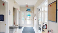 Located at 400 Hidden Ridge Ct in South Park, PA, this single-floor community amenity center offers a well-rounded set of facilities designed for recreation and relaxation. The welcoming entry hallway features white tile flooring, a drinking fountain, and glass-paneled doors that provide views of the outdoor pool area, setting a bright and functional tone throughout.

The spacious living room boasts soaring vaulted ceilings, a ceiling fan, and an abundance of natural light streaming through large arched and standard windows adorned with decorative valances. Rich leather seating, track lighting, and a wall-mounted HVAC unit complete this comfortable gathering space. An adjacent multipurpose area includes a kitchenette with light wood cabinetry, a microwave, sink, and compact appliances, alongside a wall-mounted television and casual seating.

The well-equipped exercise room features vaulted ceilings with prominent arched windows that flood the space with natural light. It houses a multi-station cable machine, treadmills, ellipticals, and a stationary bike on comfortable carpeted flooring. Three accessible bathrooms with tile flooring, grab bars, and modern vanities serve the facility. Outdoors, a generously sized swimming pool is surrounded by lounge chairs, umbrellas, and lush green landscaping, offering a pleasant retreat for residents.