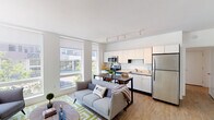 Located at 2005 Lyndale Ave S in Minneapolis, this single-floor residence offers a thoughtfully designed open-concept layout that integrates the living, dining, and kitchen areas into one cohesive space. Large floor-to-ceiling windows flood the living area with natural light and provide views of the surrounding Lyndale neighborhood streetscape, creating a bright and airy atmosphere throughout the day.

The kitchen is outfitted with stainless steel appliances, including a range, microwave, dishwasher, and refrigerator, complemented by crisp white cabinetry that extends to the ceiling for ample storage. Light-toned countertops and wood-look flooring tie the kitchen seamlessly into the adjoining living and dining space.

The living area is generously proportioned, accommodating a full seating arrangement with room for a dining table nearby. Track lighting runs along the ceiling, providing flexible illumination across the open-plan zone.

The bedroom is a calm, well-proportioned retreat featuring dual windows with roller shades that offer city views while maintaining privacy. Neutral walls and carpeted flooring contribute to a restful environment.

The bathroom features wood-look flooring, white tile surround in the shower/tub area, and clean, minimalist fixtures consistent with the modern aesthetic carried throughout the unit.