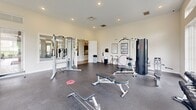 Located at 3001 Summit Dr in South Park, PA, this fitness center offers a single-floor exercise room designed to support a comprehensive workout experience. The space is defined by its bright, open feel, thanks to an expansive wall of large floor-to-ceiling windows and transom windows above, which flood the room with natural light and frame picturesque views of the surrounding green hillside and community grounds.

The exercise room features durable rubber flooring throughout, providing a safe and practical surface for a wide range of activities. Cardio equipment includes multiple Life Fitness treadmills and a stationary bike, conveniently positioned near the windows to take advantage of the outdoor scenery. A wall-mounted flat-screen television adds an entertainment option for users during cardio sessions.

Strength training is well-supported with a multi-station cable machine, a dedicated free weight area stocked with a full rack of dumbbells in varying sizes, and an adjustable workout bench. Additional equipment includes a hula hoop and resistance accessories for flexibility and functional training. Framed exercise reference charts are mounted on the walls as a helpful resource.

The room is finished with recessed lighting, neutral-toned walls, and a clean, uncluttered layout that maximizes usable floor space. The overall ambiance is bright, welcoming, and purposefully designed to encourage an effective fitness routine.
