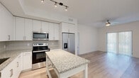 Located at 6180 Rock Island Road in Tamarac, Florida, this single-floor, 2-bedroom, 1-bathroom unit offers a clean, modern aesthetic throughout. Light wood-style flooring runs continuously across all living areas, creating a cohesive and airy feel. The kitchen is well-appointed with white shaker-style cabinetry extending to the ceiling, a gray subway tile backsplash, granite countertops, and a full suite of stainless steel appliances including a side-by-side refrigerator with ice maker, an electric range, a microwave, and a dishwasher. Track lighting illuminates the workspace, and a central kitchen island with a granite top provides additional prep space. The open living area benefits from abundant natural light through a large sliding glass door fitted with vertical blinds, and is finished with a ceiling fan overhead. Both bedrooms are comfortably sized, with the primary bedroom featuring a ceiling fan, a window with natural light, and access to a hallway lined with generous closet space. The shared full bathroom includes a tiled tub-shower combination with chrome fixtures. The clean white walls and neutral palette throughout give the space a bright, move-in-ready character.