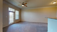 This single-floor residence offers a well-designed layout that balances comfort and functionality. The living area is generously proportioned, featuring plush wall-to-wall carpeting, crown molding along the ceiling, and a ceiling fan with a light fixture. A glass-paneled door with transom window floods the space with natural light and provides access to the outdoors, offering pleasant exterior views.

The kitchen is designed for practicality, showcasing rich dark wood cabinetry, granite-style countertops, and a full suite of black and stainless steel appliances including a refrigerator, range, and microwave. Light-toned ceramic tile flooring, a tile backsplash, and track lighting complete the kitchen's clean aesthetic. A breakfast bar with pendant lighting connects the kitchen seamlessly to the living and dining area, making it ideal for both casual dining and entertaining.

The bedroom is a comfortable, carpet-floored retreat with a ceiling fan, neutral walls, and ample space. The full bathroom features tile flooring, a dark wood vanity with a single sink, a framed mirror, and a separate shower/tub area, providing a clean and functional layout. Crown molding carries throughout, lending a cohesive, polished character to the entire residence.