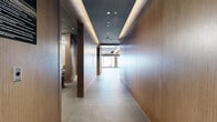 Located at 70 Nicholas St in Ottawa's downtown core, this modern fitness facility is thoughtfully designed to accommodate a wide range of exercise disciplines. The space spans a generous single floor and is organized into several distinct zones connected by well-appointed hallways. The main exercise area is a standout, featuring large floor-to-ceiling windows that flood the room with natural light and offer views of the surrounding cityscape. Rows of treadmills and cardio machines are positioned along the window wall, while an adjacent strength training zone provides adjustable benches, a full dumbbell rack, power racks, and turf sled tracks. Warm wood-paneled walls and large mirrors create a polished, professional atmosphere throughout. A dedicated studio room offers hardwood flooring, wall-to-wall mirrors, a mounted flat-screen display, and yoga mats with blocks, making it ideal for yoga, stretching, or group classes. Cycling stations and additional cardio equipment are housed in a separate glass-partitioned area. Recessed and circular pendant lighting throughout ensures consistent, flattering illumination across all zones. The facility also includes a lounge area and multiple hallways that provide smooth circulation between zones, completing a well-rounded, premium fitness environment.