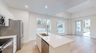 Located at 11 Wright Cres in Kingston, Ontario, this thoughtfully designed 2-bedroom, 2-bathroom unit offers a clean, modern aesthetic across a single floor. Light-toned hardwood flooring flows consistently throughout, complementing the crisp white walls and trim that define the interior.

The open-concept kitchen and living area serves as the heart of the unit. The kitchen features white shaker cabinetry, a white quartz waterfall island with a double stainless steel sink, a white subway tile backsplash, and a full suite of stainless steel appliances including a refrigerator, electric range, and built-in microwave. A large window bathes the kitchen in natural light. The adjoining living area is bright and airy, with multiple large windows and a glass-panel exterior door that opens to the outdoors.

A well-lit hallway connects the living spaces to the private quarters, where two bedrooms offer comfortable proportions and generous natural light through sizeable windows. The primary bedroom provides direct access to its own bathroom. Both bathrooms are finished in a clean, contemporary style, with one featuring a walk-in glass sliding shower enclosure.

A dedicated laundry area houses a stacked Whirlpool washer and dryer. The overall ambiance is fresh, bright, and move-in ready.