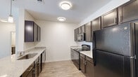 This single-floor residence offers a thoughtfully designed open-concept layout that seamlessly connects the living and kitchen areas. The kitchen is a standout feature, equipped with dark espresso cabinetry, light granite-style countertops, black appliances including a refrigerator, electric range, built-in microwave, and dishwasher, all set atop light wood-style flooring. A breakfast bar with pendant lighting bridges the kitchen to the living space, enhancing the open feel. The living area is bright and spacious, featuring wood-style flooring, a ceiling fan, and French doors that open to a private balcony, inviting natural light and outdoor views. Bedrooms are generously sized, with wood-style floors, ceiling fans, and large windows that allow ample natural light. The bathrooms are finished with large-format light tile flooring, dark vanity cabinetry, granite-style countertops with undermount sinks, and soaking tubs with white subway tile surround. Clean white walls and neutral tones throughout the residence create a cohesive, modern aesthetic that is both functional and inviting.