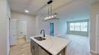 This contemporary 640 square foot apartment in Elgin, IL, offers a thoughtful blend of style and functionality. The open-concept design maximizes space, seamlessly connecting the living area and kitchen. The kitchen is a standout feature, boasting sleek white cabinetry contrasted with lower gray cabinets, stainless steel appliances, and a large central island with a modern pendant light fixture. Light wood flooring throughout the main living areas adds warmth and continuity.

The spacious bedroom, measuring 150 square feet, features plush carpeting and a large window, ensuring ample natural light. The bathroom is well-appointed with a single vanity, ample counter space, and modern fixtures. Throughout the apartment, recessed lighting and large windows create a bright, airy atmosphere. The unit also includes in-unit laundry facilities for added convenience.

Storage is thoughtfully integrated, with closets featuring white panel doors. The overall color palette of whites and light grays contributes to the apartment's modern, clean aesthetic. This efficient one-bedroom layout offers comfortable living in a contemporary setting, ideal for those seeking a stylish urban lifestyle.