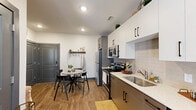 This single-floor unit offers a thoughtfully designed layout accommodating three bedrooms and three bathrooms. The kitchen features a clean, modern aesthetic with two-tone cabinetry—white upper cabinets and taupe lower cabinets—paired with light quartz countertops, a tile backsplash, and stainless steel appliances including a range, microwave, and refrigerator. A compact dining area adjacent to the kitchen provides convenient everyday functionality.

The living room is bright and welcoming, benefiting from natural light via large sliding glass doors that open to an outdoor space. A ceiling fan overhead and wood-style flooring underfoot contribute to the room's comfortable ambiance. A dedicated reading nook beside the patio doors adds a practical secondary seating area.

Each bedroom features a ceiling fan, natural light from windows with exterior views, and wood-style flooring. The primary bedroom is cozy and efficiently sized. The additional bedrooms are similarly compact, with one featuring a built-in desk area suited for work or study.

All three bathrooms maintain a consistent design language, incorporating taupe vanities with quartz countertops, black hardware accents, white tile tub-shower combinations, and wood-style flooring, delivering a cohesive and polished finish throughout the unit.