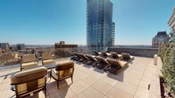 Located at 1401 Spruce Street in Philadelphia's Center City neighborhood, this sophisticated rooftop terrace offers a remarkable open-air retreat high above the urban landscape. The terrace is finished with large-format, travertine-style tile pavers that lend a clean, upscale aesthetic throughout the outdoor space. Panoramic, unobstructed views of the Philadelphia skyline stretch in multiple directions, with neighboring high-rise towers and the broader cityscape visible under open skies.

The terrace is thoughtfully arranged with multiple seating zones, including cushioned lounge chairs and side tables ideal for conversation or relaxation, as well as a dedicated sun-bathing area furnished with rows of padded chaise lounges. A decorative pergola draped in lush greenery adds a refined architectural accent, while raised planters featuring sculpted shrubs and climbing foliage introduce natural elements that soften the hardscape. Glass panel railings along the perimeter preserve sightlines while ensuring safety.

Interior access is provided through floor-to-ceiling glass doors, connecting the terrace to an enclosed indoor area with recessed lighting and tiled flooring, allowing seamless indoor-outdoor transition. The combination of generous open space, stylish furnishings, verdant landscaping, and commanding city views makes this rooftop terrace an exceptional amenity in the heart of Philadelphia.