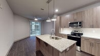 Located at 1717 South Riverside Drive in Tulsa, Oklahoma, this single-floor unit presents a thoughtfully designed contemporary living space. The open-concept layout connects the kitchen and living areas seamlessly, creating an inviting and functional flow throughout.

The kitchen serves as a central highlight, anchored by a large island topped with speckled granite countertops and an undermount sink with an industrial-style faucet. Warm wood-tone cabinetry extends floor-to-ceiling, offering generous storage, while stainless steel appliances — including an electric range, over-the-range microwave, and refrigerator — add a polished, modern touch. Pendant lighting suspends above the island, complementing the recessed lighting throughout. Dark wood-look flooring runs through the kitchen and living area, extending toward sliding glass doors that open to an outdoor space, allowing natural light to pour in.

The bedroom is carpeted and comfortably proportioned, with a ceiling fan, a window with exterior views, and neutral gray walls that create a calm atmosphere.

The bathroom features wood-look flooring consistent with the modern aesthetic, a granite-topped floating vanity with an illuminated mirror, a tall wood-tone storage cabinet, and a tub-shower combination with gray tile surround and glass sliding doors.