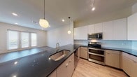 Located at 6848 Bandera Ave in the desirable 75225 zip code of Dallas, Texas, this single-floor residence showcases a clean, contemporary design throughout. The open-concept kitchen serves as the heart of the home, featuring dark granite countertops, dual-tone cabinetry with flat-panel white upper cabinets and warm wood lower cabinets, a light blue glass tile backsplash, and a full suite of stainless steel appliances including a double oven range and built-in microwave. Globe pendant lights hang overhead, adding a modern touch to the space. The kitchen flows seamlessly into the living and dining areas, which are finished with durable wood-look flooring and neutral-toned walls that lend a bright, airy feel. A set of French doors with sidelights invites abundant natural light into the living area and provides outdoor access. The bedrooms are carpeted for comfort, each offering generous natural light through large windows with blinds and ceiling fans for year-round comfort. The bathroom is well-designed, featuring a wide vanity with a white countertop, wood-toned cabinetry, a large mirror, and a tiled bathtub and shower combination. Wood-look flooring continues throughout the bathroom, tying the overall aesthetic together cohesively.