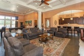 Located at 5300 Antequera Rd NW in Albuquerque, New Mexico, this single-floor space exudes a warm Southwest-inspired elegance throughout its well-appointed interior. The entryway welcomes visitors with rich dark tile flooring, a classic patterned area rug, and a pair of leather armchairs accented with nailhead trim, all set against warm terracotta-toned walls and white-trimmed windows that invite natural light.

The main living area opens into a generous, light-filled room with elevated tray ceilings detailed with crown molding, recessed lighting, and decorative columns that define the space. Large windows fitted with drapery panels frame views to the outdoors, while hardwood flooring adds warmth underfoot. The seating arrangement centers around a substantial leather sofa and coordinating chairs, styled with decorative pillows for a comfortable yet refined atmosphere.

A standout feature is the floor-to-ceiling stacked-stone fireplace, lending a rustic, architectural focal point to the room. Adjacent windows offer views of an outdoor patio and pool area beyond. A graceful arched passageway leads to a wet bar area appointed with dark wood cabinetry, granite countertops, pendant lighting, and bar seating — ideal for entertaining. Throughout, the cohesive design palette of warm neutrals and rich dark furnishings creates an inviting and sophisticated ambiance.