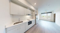 Located at 3803 S Warsaw St in Seattle's vibrant Columbia City neighborhood, this efficient one-bedroom, one-bathroom unit offers a well-designed layout across a single floor. The interior features a clean, modern aesthetic throughout, with light gray wood-style flooring and crisp white walls that create a bright, cohesive atmosphere.

The galley-style kitchen is thoughtfully appointed with white flat-front cabinetry, open shelving, a white quartz countertop, a stainless steel sink, an electric cooktop, a built-in microwave, and a full-size refrigerator — maximizing both function and storage in a compact footprint.

The kitchen flows into an open living area anchored by a large picture window fitted with a roller shade, allowing an abundance of natural light and providing elevated views of the surrounding Seattle neighborhood. A ceiling fan adds comfort to the living space.

The bedroom is a well-proportioned private retreat featuring the same light hardwood-style flooring, neutral walls, and a generously sized window with outdoor views and a roller shade for privacy.

The bathroom is finished in a clean, minimalist style with a floating vanity, large mirror with overhead lighting, a walk-in shower, and wood-tone tile flooring — all in a bright white palette that enhances the sense of space.