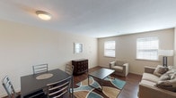 This 2-bedroom, 2-bathroom flat is a well-appointed single-floor residence offering a practical and comfortable layout. The living area is generously sized, featuring rich dark hardwood flooring, neutral warm-toned walls, and multiple windows that allow natural light to fill the space. The open arrangement accommodates both a dining area and a sitting area, making it ideal for everyday living and entertaining.

The kitchen is equipped with warm wood cabinetry, stone-patterned countertops, a textured backsplash, and a stainless steel sink, providing ample storage and workspace for meal preparation.

Both bedrooms are carpeted and well-proportioned. The primary bedroom features a ceiling fan with light fixture, multiple windows with blinds, and sufficient space for a full furniture arrangement. The second bedroom also includes a ceiling fan, a window for natural light, and comfortable proportions suitable for rest or a guest room.

The bathrooms are finished with stone-patterned countertops, an undermount sink, and a well-lit vanity mirror with a multi-bulb fixture, contributing to a clean and functional aesthetic.

Throughout the flat, the design maintains a cohesive, neutral palette with consistent finishes that create a calm and inviting atmosphere across all rooms.