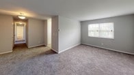 This single-floor unit offers a straightforward and functional layout designed for comfortable everyday living. The floor plan, as seen in the 3D overview, includes a generously sized main living area that flows into adjacent rooms, providing a cohesive and accessible arrangement throughout.

The living spaces feature neutral gray walls and plush wall-to-wall carpeting, creating a clean and understated aesthetic. Multiple rooms are bright and open, with windows fitted with blinds that allow natural light to filter in while maintaining privacy. Each carpeted room offers ample space and clean lines, suitable for a variety of uses.

The kitchen is equipped with warm-toned wooden cabinetry, granite-style countertops, and a black gas range with a ventilation hood above. A window above the counter area brings in natural light, and the stone-tile flooring adds a durable, practical finish to the space.

The full bathroom features a soaking tub with a shower surround, chrome fixtures and hardware, a wooden vanity, and stone-look tile flooring. A second, half bathroom includes a pedestal-style sink, toilet, large mirror, and white tile flooring, offering added convenience for residents and guests alike.

Overall, this unit presents a clean, move-in-ready environment with consistent finishes, functional amenities, and a well-organized single-level layout.