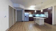This well-designed single-floor residence showcases a contemporary aesthetic throughout, blending modern finishes with functional living spaces. The kitchen serves as a standout centerpiece, featuring rich dark-espresso cabinetry extending to the ceiling, crisp white countertops, a mosaic tile backsplash in neutral tones of gray and blue, and a full suite of stainless steel appliances including a French door refrigerator with ice maker, range, microwave, and dishwasher. A peninsula island with pendant lighting overhead provides additional prep space and casual seating. Wood-look plank flooring flows seamlessly through the kitchen and into the open living area, which benefits from natural light through a window and sliding glass door leading to an outdoor balcony, complemented by a ceiling fan above. The bedrooms offer plush carpeting underfoot, ceiling fans, and direct access to generously sized walk-in closets with built-in shelving systems. Two bathrooms serve the residence: one featuring large-format light tile flooring, dark cabinetry with a single vanity, and a separate accessible shower area; the other showcasing gray large-format tile, a glass-enclosed corner shower with marble-accented threshold, and clean, minimalist finishes. Throughout, gray-painted doors and trim create a cohesive, modern design language.