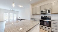 Located at 1535 Newbridge Dr in Kernersville, NC, this well-appointed single-story home offers three bedrooms, two bathrooms, and a thoughtfully designed open-concept layout. The kitchen and living room flow seamlessly together, anchored by a large center island with granite countertops and an integrated sink. Grey shaker-style cabinetry, a classic subway tile backsplash, and a full suite of stainless steel appliances—including a refrigerator, range, microwave, and dishwasher—complete the kitchen. Pendant lighting above the island and recessed lighting add a polished finishing touch. The living area features light luxury vinyl plank flooring, a ceiling fan, and glass double doors that invite natural light and provide outdoor views. The bedrooms are carpeted for comfort; the primary bedroom is generously sized with direct access to a dedicated closet and a private en-suite bathroom. Additional bedrooms offer clean, neutral spaces with ample room. The bathrooms are finished with warm brushed-gold fixtures and clean white surrounds. A dedicated laundry area houses a full-size washer and dryer. Three closets throughout the home provide practical storage. The clean, neutral color palette and modern finishes give the entire space a fresh, move-in-ready feel.