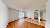 This single-floor unit offers a straightforward, functional layout with a clean and bright interior throughout. The living area is a standout space, featuring warm hardwood-style flooring that extends across the main living zones, crisp white walls, and a textured ceiling. A full-length sliding glass door dressed with vertical blinds floods the room with natural light and provides outdoor access, casting attractive light patterns across the floor. The open feel of the living area is complemented by a dedicated entryway with a solid white door.

The kitchen is a compact yet practical galley-style space, outfitted with classic wood cabinetry, a white electric range, a stainless steel sink with light countertops, and a window with vertical blinds that brings in additional natural light. The hardwood-style flooring continues seamlessly into this area.

The bedroom offers a quieter, cozier atmosphere with plush neutral carpet, white walls, a textured ceiling, and a large window with vertical blinds that frame views of surrounding greenery, allowing ample natural light to filter in.

The bathroom is finished with a clean, all-white tub and shower combo featuring tiled surround walls and chrome fixtures, maintaining the unit's consistent, no-fuss aesthetic throughout.