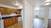 This one-bedroom, one-bathroom unit in the Fields neighborhood of Indianapolis offers a well-organized single-floor layout designed for efficient, comfortable living. The living room serves as the central gathering space, featuring light wood-tone laminate flooring, crisp white walls, and two windows that invite natural light and views of the surrounding neighborhood. A wall-unit air conditioner provides climate control directly in the living area.

The kitchen connects to the living room through a open doorway and is outfitted with warm honey-toned wood cabinetry, dark countertops, a double-basin sink, a dishwasher, and a range. Tile flooring anchors the kitchen's practical character. A hallway links the main living areas to the private spaces, including a dedicated closet for additional storage.

The bedroom is a comfortable, carpet-floored retreat with white walls, a window bringing in natural light, and a quiet, restful ambiance. The bathroom features a matching wood vanity with a light countertop, a large mirror, tile flooring, a bathtub, and clean white fixtures. Throughout the unit, the neutral color palette and consistent finishes create a cohesive, move-in-ready atmosphere.