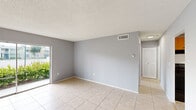 Located at 401 Executive Center Dr in West Palm Beach, FL, this one-bedroom, one-bathroom unit offers a practical and functional single-floor layout. Light neutral gray walls and large-format tile flooring run consistently throughout the space, creating a cohesive and easy-to-maintain interior.

The open living room provides a generous amount of space and is bathed in natural light via a sliding glass door that opens to the outdoors. A textured ceiling adds subtle architectural character to the room. The kitchen is efficiently designed, featuring warm wood-toned cabinetry that extends to the upper and lower levels, white countertops, a stainless steel sink, and black appliances including a refrigerator, range, and dishwasher. A flush-mounted ceiling light provides focused illumination in the kitchen area.

The spacious bedroom includes a louvered closet door and a window that brings in natural light with views of the surrounding greenery. The bathroom is finished with full-height beige tile surrounding a bathtub and shower combination, complemented by clean white fixtures. A louvered door accents the bathroom entry as well, maintaining a consistent design theme throughout the unit.