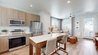 This thoughtfully designed 1-bedroom, 1-bathroom residence offers a cohesive, modern aesthetic across a single floor. Light wood-style flooring flows seamlessly throughout, tying together each room with a warm, contemporary feel.

The open-concept kitchen and living area forms the heart of the space. The kitchen is outfitted with light wood cabinetry, white quartz countertops, and a full suite of stainless steel appliances, including a range, microwave, and refrigerator. A freestanding dining table with a marble-look top serves as both a dining and gathering area. The adjacent living room benefits from multiple windows that invite abundant natural light, complemented by a ceiling fan and access to an exterior door. A built-in wall shelf with an integrated workspace adds functional versatility.

The bedroom is a calm, well-proportioned retreat featuring a window with views, a ceiling fan, and direct access to both a dedicated closet and the bathroom. The closet provides ample storage with full shelving and hanging space.

The bathroom is clean and modern, featuring wood-tone cabinetry, a white quartz vanity, a glass-enclosed shower, and open wall shelving for added storage. A hallway connects the main living areas to the private quarters, completing the efficient and functional layout of this well-appointed residence.