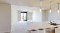 Located at 3003 Olin Ave in San Jose, CA, this modern one-bedroom, one-bathroom residence offers a well-designed single-floor layout with a bright, contemporary aesthetic throughout. The open-concept living and kitchen area forms the heart of the home, where warm hardwood flooring anchors a sleek kitchen equipped with stainless steel appliances — including a French door refrigerator, built-in oven, microwave, and a wine cooler — complemented by wood-grain cabinetry and clean white countertops. A peninsula with pendant lighting separates the kitchen from the spacious carpeted living area, which extends toward a sliding glass door leading to a private balcony. The bedroom is comfortably sized with soft carpet flooring, large windows that invite natural light and outdoor views, and access to a dedicated walk-in closet with wire shelving for ample storage. The full bathroom features tile flooring, a wood-finish vanity with an integrated sink, a large mirror, and a tub-shower combination with clean white tile surround. Neutral tones, recessed lighting, and modern finishes throughout lend the space a cohesive, move-in-ready ambiance suited for comfortable urban living.
