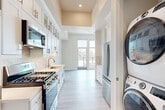This thoughtfully designed single-floor residence accommodates four bedrooms and one bathroom within a well-organized layout that maximizes every square foot. The galley-style kitchen is a standout feature, outfitted with crisp white shaker cabinetry — including glass-front upper cabinets — a subway tile backsplash, quartz countertops, a stainless steel gas range, built-in microwave, and a large French door refrigerator. A stacked washer and dryer unit is conveniently integrated near the kitchen. Light wood-toned flooring runs throughout the entire unit, lending a clean, cohesive aesthetic. The primary bedroom is generously proportioned, featuring floor-to-ceiling windows that open to a private balcony with open urban and neighborhood views. Additional bedrooms are bright and airy, benefiting from natural light through modern windows. The bathroom is finished with large-format wall tiles, a glass-enclosed walk-in shower, a white vanity with quartz countertops, and an LED-backlit mirror. A tray ceiling detail in the kitchen adds an architectural touch, while recessed lighting and a neutral color palette maintain the home's clean, contemporary ambiance throughout.