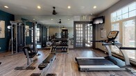 Located along I-25 in Castle Rock, Colorado, this fitness center offers a thoughtfully designed workout facility that caters to a wide range of exercise needs. The space is organized across a single floor and is divided into distinct functional zones, each outfitted with professional-grade equipment.

The cardio area is bathed in natural light from a generous row of large windows, offering views of the surrounding outdoor environment. Treadmills, elliptical machines, and a rowing machine are arranged to take full advantage of this bright, airy atmosphere, complemented by ceiling fans and wall-mounted televisions. Durable wood-look flooring runs throughout, adding warmth to the space.

The strength training section features a full dumbbell rack, weight benches, and multiple TKO cable and resistance machines positioned against a deep teal accent wall adorned with contemporary artwork. Floor-to-ceiling mirrors expand the sense of space and allow users to monitor their form. Recessed lighting and ceiling fans maintain a comfortable environment throughout.

Entry to the fitness center is made through sleek frosted glass sliding doors, creating a polished, modern transition into the facility. Restroom access is conveniently located near the entrance. The overall design balances functionality with a clean, contemporary aesthetic, making this a well-appointed destination for fitness in Castle Rock.
