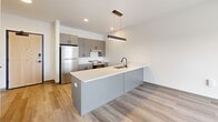 Located at 2132 Stokes Blvd in Cleveland's vibrant University Circle neighborhood, this thoughtfully designed one-bedroom, one-bathroom residence offers a modern aesthetic throughout its efficiently laid-out single floor. The open-concept living, dining, and kitchen area serves as the heart of the unit, anchored by a sleek kitchen island with a white quartz countertop, an undermount sink with a matte black faucet, and built-in microwave. Cabinetry in a contemporary gray-taupe finish pairs with stainless steel appliances, including a refrigerator and range, set against a clean white tile backsplash. Pendant lighting and recessed fixtures illuminate the space warmly. Light wood-tone flooring flows consistently throughout, complementing the bright, neutral palette. The living area extends toward a sliding glass door that opens to a balcony with open city views. The spacious bedroom features large floor-to-ceiling windows framing panoramic Cleveland skyline views, along with generous closet space across multiple built-in closets. The bathroom is finished with elegant herringbone-patterned marble-look tile flooring, a floating vanity, and matte black hardware accents. In-unit laundry adds everyday convenience to this clean, contemporary residence.