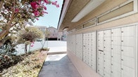 This single-story property showcases a classic Southwestern-inspired architectural style, characterized by textured stucco exterior walls finished in warm earth tones and a tiled roofline that adds a touch of traditional charm. The exterior is enhanced by eye-catching mint-green metal railings that line the entry steps, providing both safety and a pop of color against the neutral facade. Arched architectural details contribute to the building's distinctive character, while mature flowering trees — including a vivid bougainvillea bursting with pink blooms — lend vibrant natural color to the surroundings and complement the sun-drenched setting.

The grounds are designed with functionality in mind. A centralized mailbox area is prominently featured, housing a large bank of individual metal mailboxes neatly organized along a covered, open-air corridor. This communal facility serves the building's residents efficiently and is easily accessible from the main walkway. The wide concrete pathways throughout the exterior provide ample circulation space and contribute to the overall open, airy feel of the property.

With its cheerful landscaping, warm stucco finishes, and well-maintained common areas, this property presents a welcoming and cohesive aesthetic well-suited to its sunny climate.