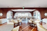 Located at 625 E Dania Beach Blvd in Dania Beach, Florida, this elegantly designed clubroom delivers a refined social environment that blends nautical-inspired aesthetics with modern sophistication. The single-floor layout encompasses a generous open footprint, unified by gleaming rich hardwood flooring with light inlay accents that runs throughout the entire space.

Distinctive dark wood-paneled archways frame the room's key zones, creating a sense of architectural depth and seamless flow. A dedicated lounge area features a plush white sectional sofa, classic tufted leather Barcelona-style chairs, a marble-topped coffee table, and a wall-mounted flat-screen TV — all anchored by a statement nautical telescope and a circular porthole mirror that reinforce the coastal theme.

The entertainment zone prominently showcases a full-sized billiards table beneath a pair of oversized pendant dome lights. Adjacent to it, a large communal high-top table with upholstered bar stools provides additional gathering space. A full-service bar with a richly grained wood facade, illuminated countertop, and elegant globe pendant lighting in gold and white serves as a central focal point.

Cream upholstered lounge chairs surround marble-topped cocktail tables throughout, while original nautical artwork adorns the walls. Floor-to-ceiling windows flood the space with natural light and frame sweeping outdoor views of the surrounding Dania Beach skyline and waterway.
