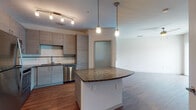 Located at 9938 Grande Lakes Blvd in Orlando, Florida, this single-floor studio unit offers a well-designed open-concept layout that maximizes functionality and flow. The kitchen serves as a central focal point, showcasing contemporary flat-front cabinetry in a warm taupe finish, a white subway tile backsplash, and a full suite of stainless steel appliances including a refrigerator, range, microwave, and dishwasher. A curved granite-topped island provides additional prep space and casual seating, illuminated by sleek pendant lights and complemented by track lighting overhead. Hardwood-style flooring extends throughout the main living and kitchen areas, adding warmth and continuity to the space. A separate bedroom features plush carpet, a ceiling fan, a window with natural light, and a louvered closet door offering ample storage. The bathroom is finished with consistent granite countertops on the vanity with gray cabinetry, a full tub-shower combination with white tile surround, and hardwood-style flooring. A hallway connects the private areas of the unit to the main living space, providing a clear and practical separation. The overall design is clean, modern, and move-in ready.